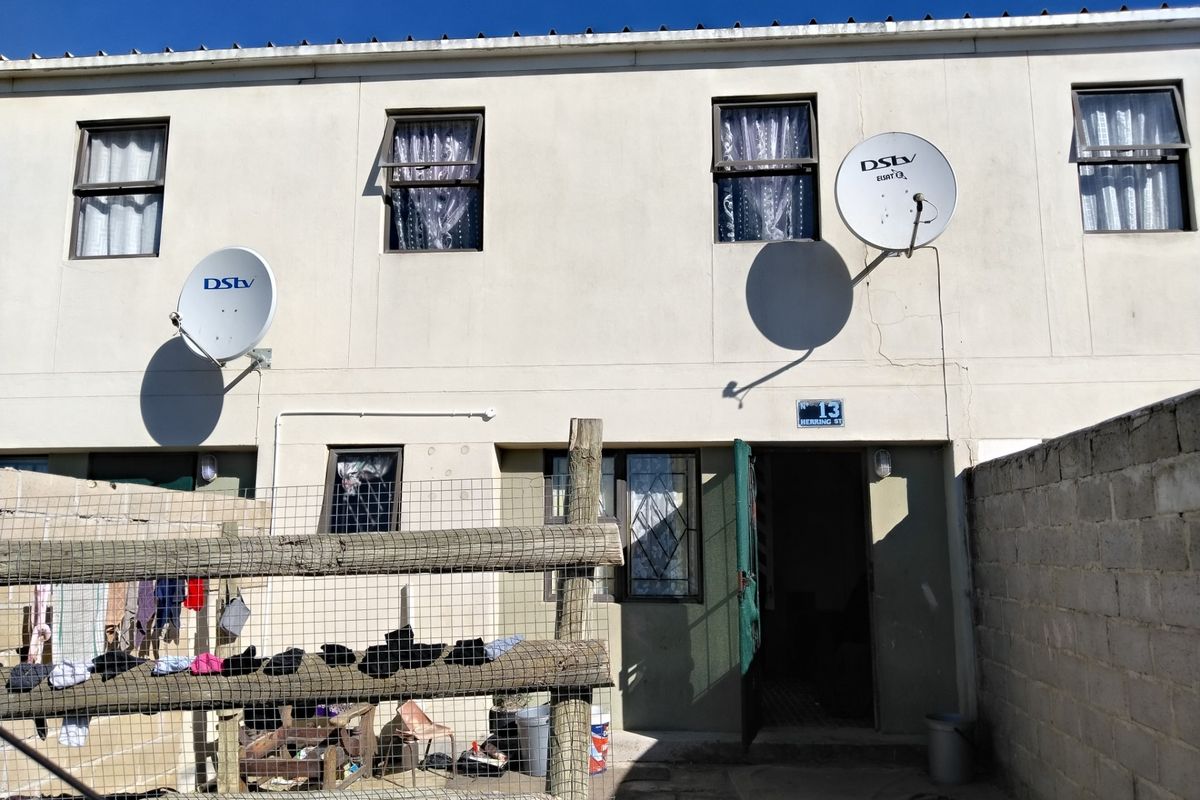 Rear exterior view of a two-story residential unit featuring satellite dishes, security gates, and a fenced outdoor area.