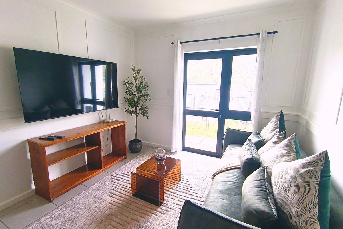 A bright living room featuring decorative wall paneling, tiled flooring, and a glass door providing access to the outdoor area.