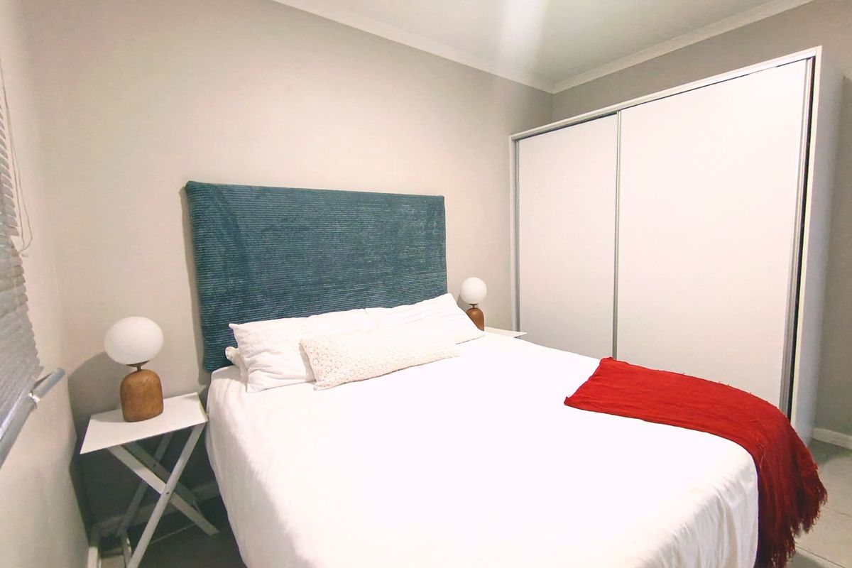 A well-maintained bedroom featuring neutral wall tones, tiled flooring, and a large built-in sliding door wardrobe.