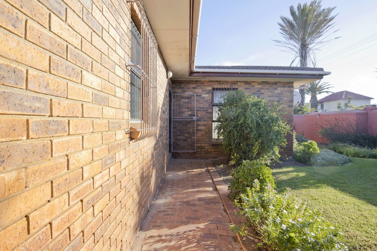 A side exterior view of the house featuring face brick walls, security bars on windows, and a paved walkway leading along the garden.