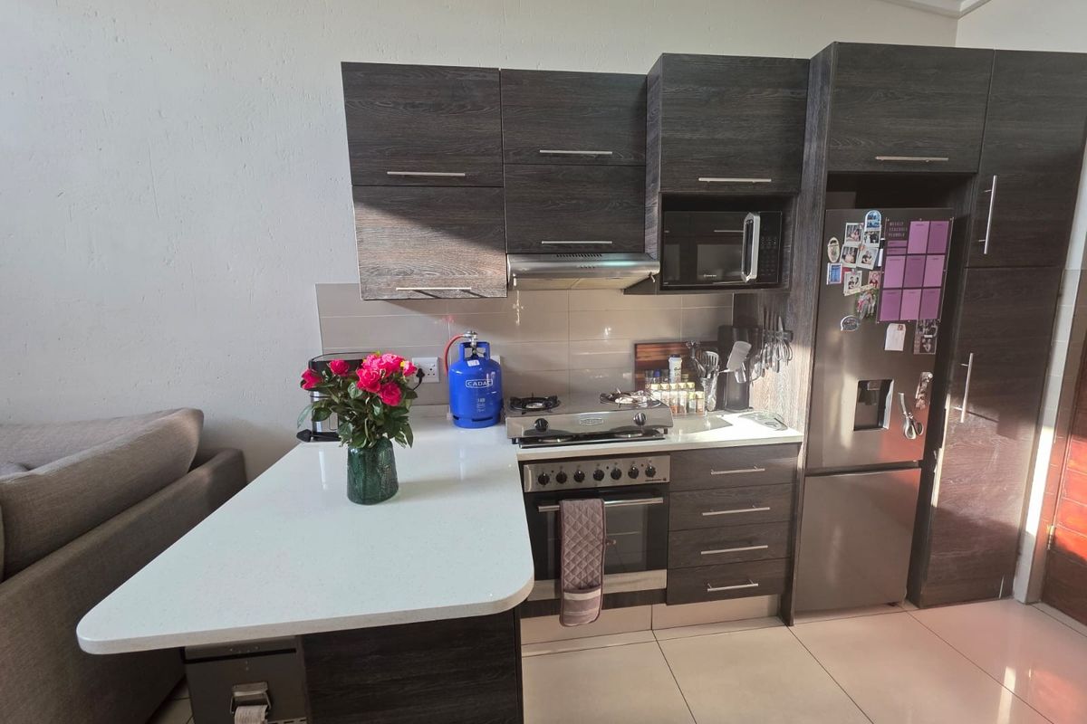 Compact modern kitchen featuring dark wood cabinetry, stone countertops, built-in oven, gas hob, and an integrated breakfast bar peninsula.