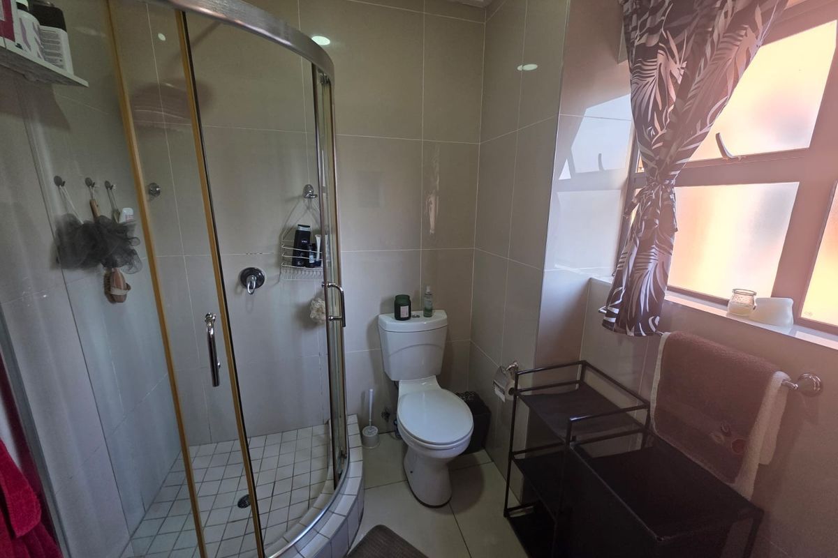 A functional bathroom featuring a corner glass shower enclosure, a standard toilet, and tiled walls and flooring with natural light from a side window.