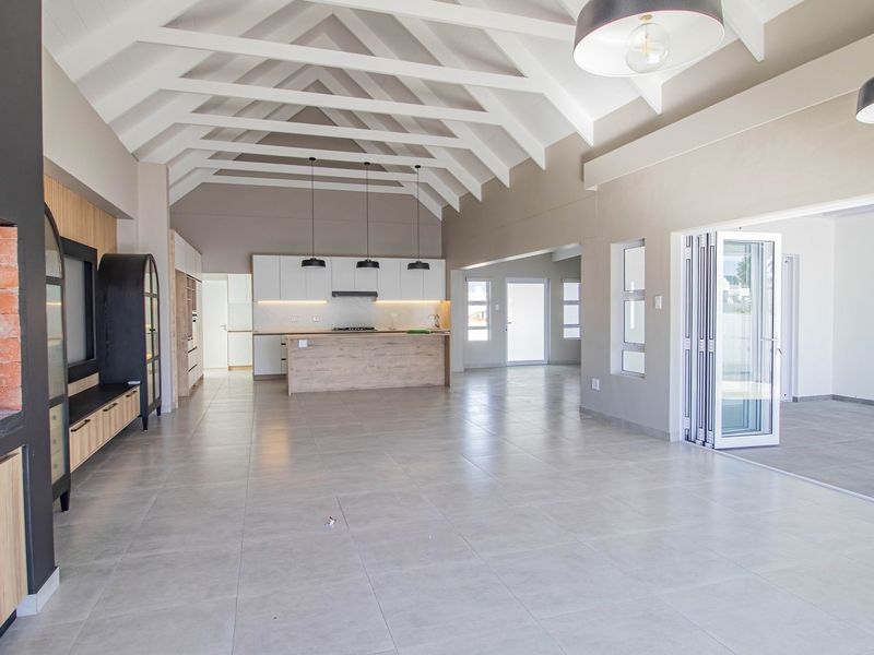 Spacious open-plan living area featuring a modern kitchen with island, vaulted exposed beam ceilings, tiled flooring, and a built-in brick fireplace.