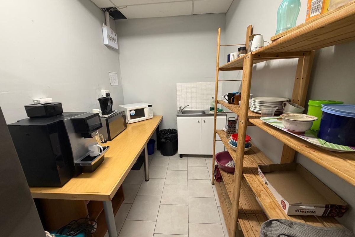 A functional office kitchenette featuring a small sink, tiled splashback, and ample counter space for appliances.