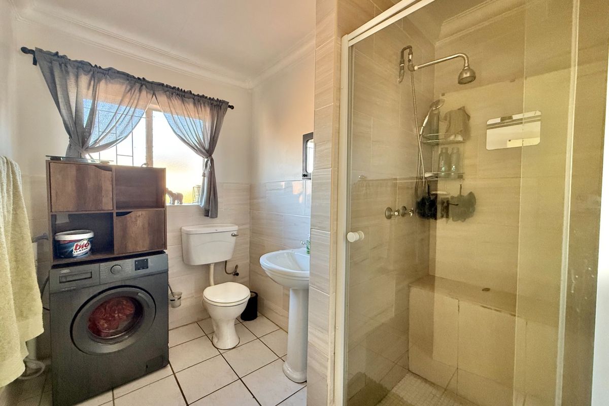 A functional bathroom featuring a glass-enclosed shower, pedestal basin, toilet, and integrated laundry space with tiled flooring and wall finishes.