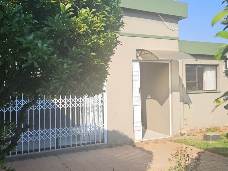 Exterior view of the property entrance featuring a security gate, paved patio area, and established garden surroundings.