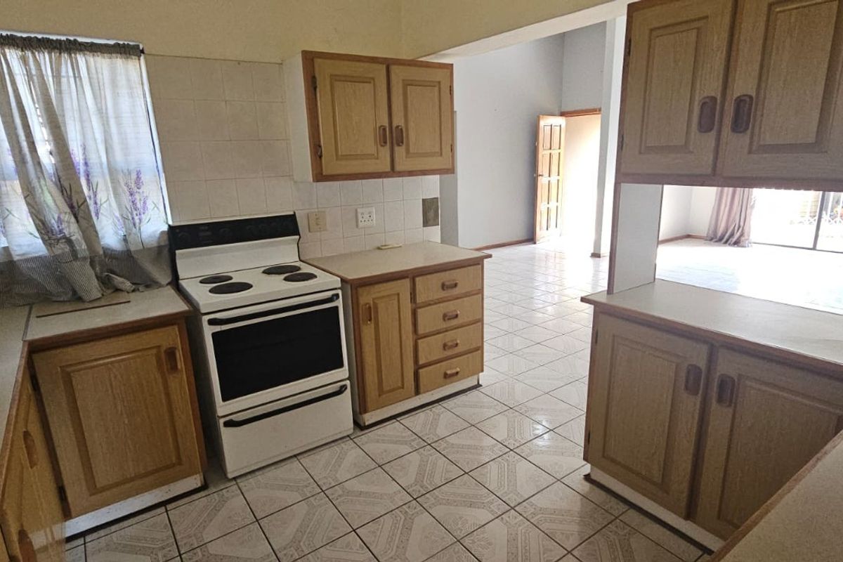 A functional kitchen featuring wooden cabinetry, tiled flooring, and a freestanding stove, with an open-plan layout leading to the living area.