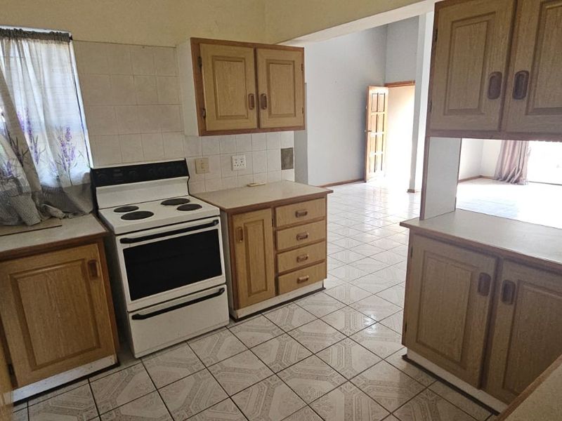 A functional kitchen featuring wooden cabinetry, tiled flooring, and a freestanding stove, with an open-plan layout leading to the living area.