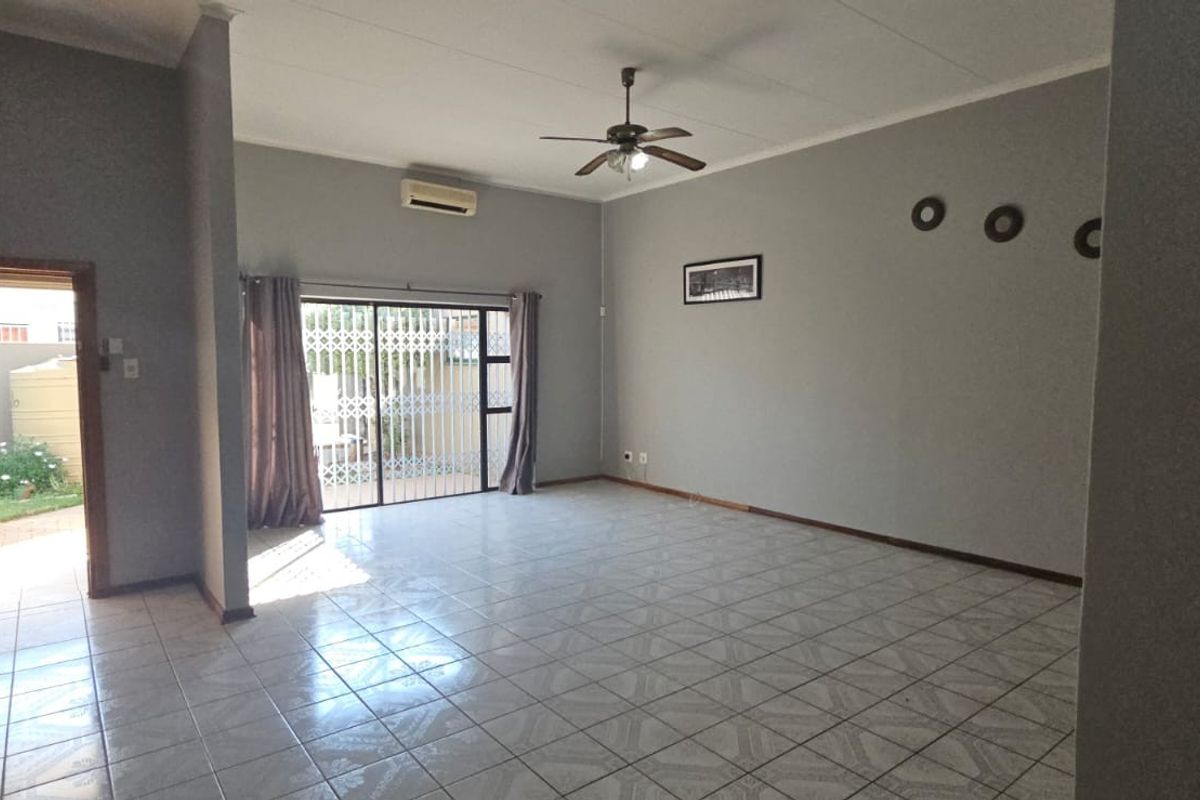 Spacious living area featuring tiled flooring, a ceiling fan, wall-mounted air conditioning unit, and sliding glass doors leading to the exterior.