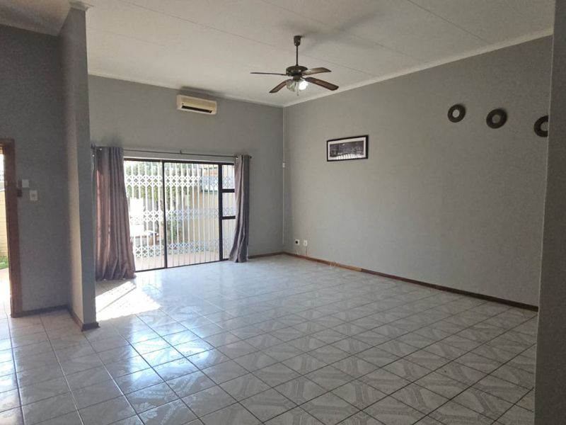 Spacious living area featuring tiled flooring, a ceiling fan, wall-mounted air conditioning unit, and sliding glass doors leading to the exterior.