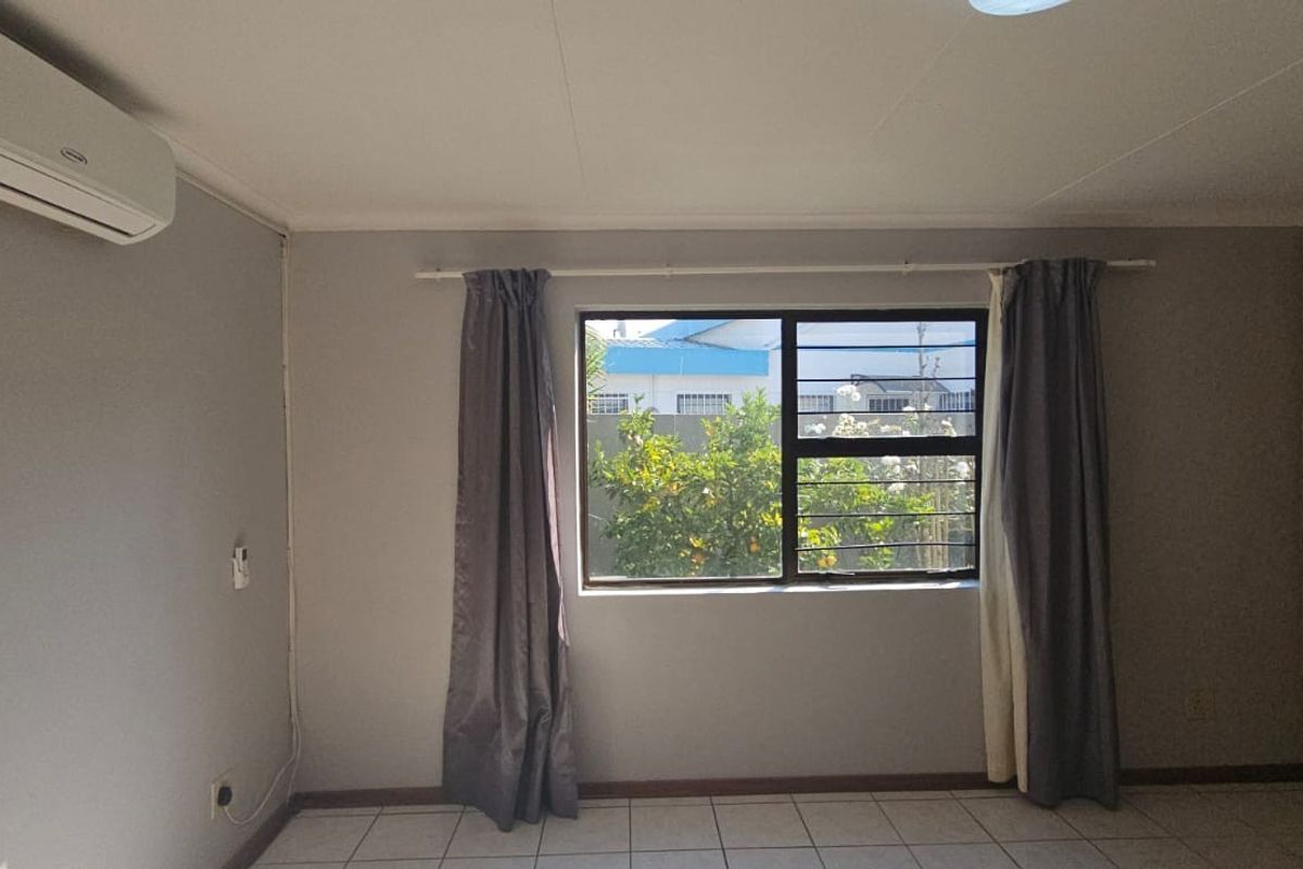 A bedroom featuring tiled flooring, a wall-mounted air conditioning unit, and built-in wooden wardrobes with a view of the garden.