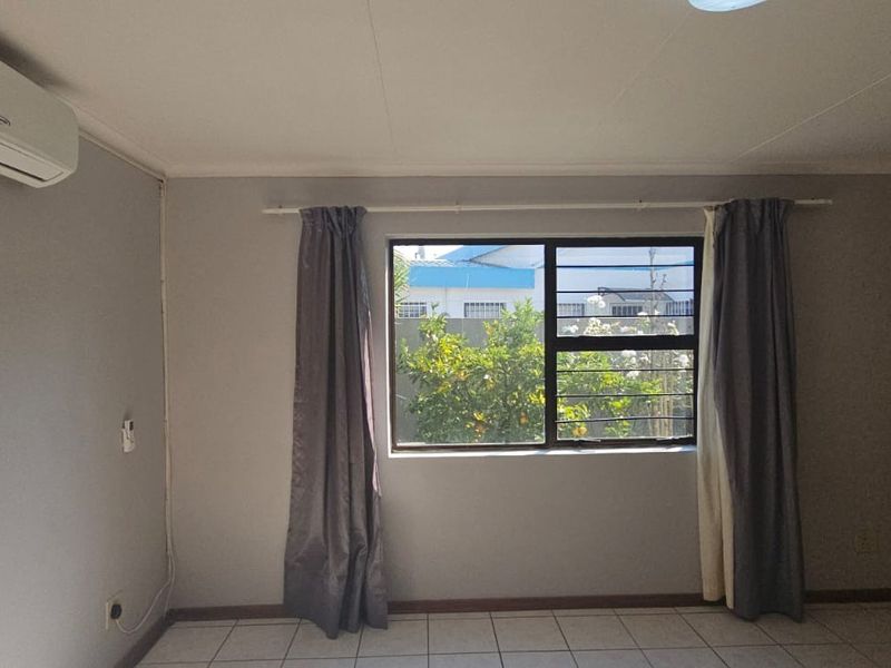 A bedroom featuring tiled flooring, a wall-mounted air conditioning unit, and built-in wooden wardrobes with a view of the garden.