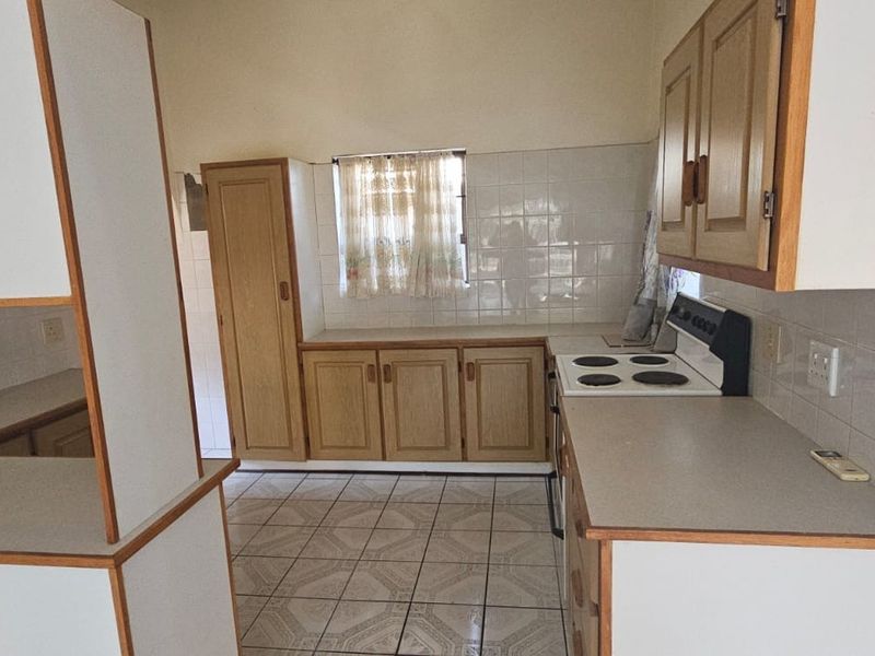 A functional kitchen featuring wooden cabinetry, tiled splashbacks, and a built-in electric stove, offering a practical layout with ample counter space.