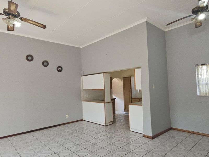 Open plan living area featuring tiled flooring, two ceiling fans, and a pass-through kitchen layout with built-in cabinetry.