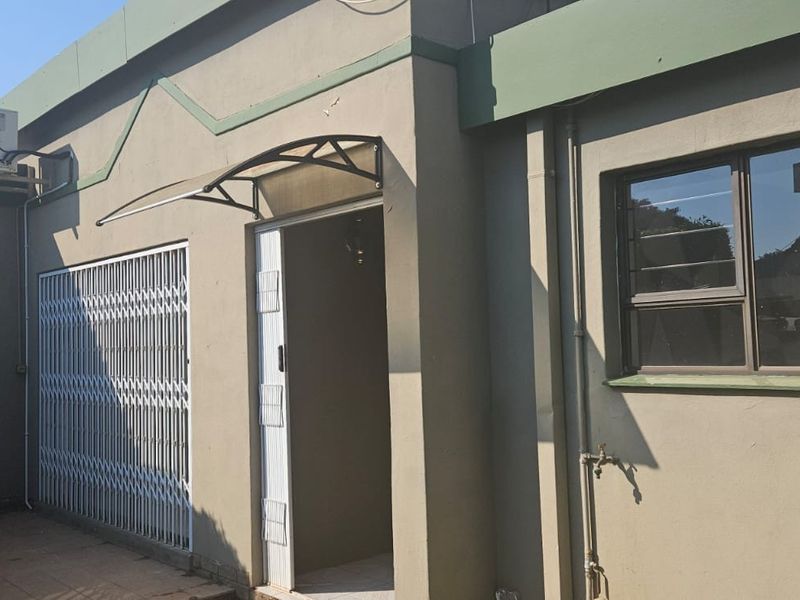 Exterior view of the property featuring a paved patio area, security gate, and wall-mounted air conditioning unit.