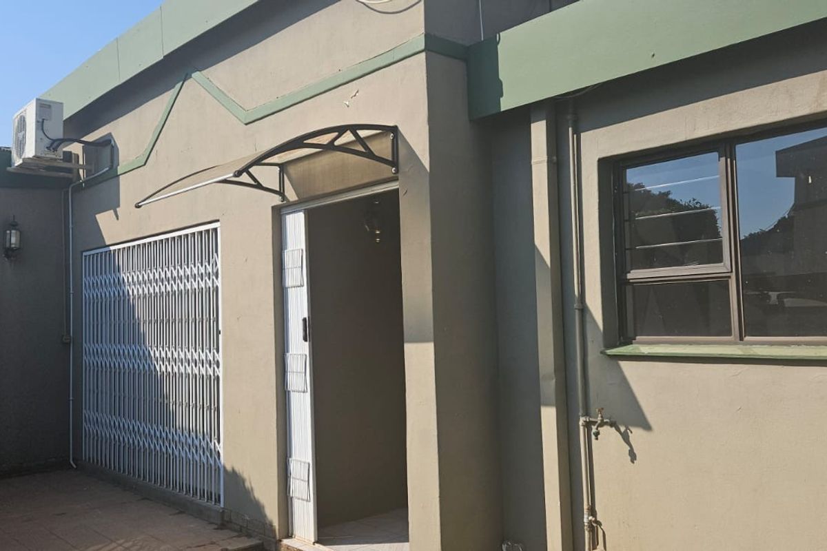 Exterior view of the property featuring a paved patio area, security gate, and wall-mounted air conditioning unit.