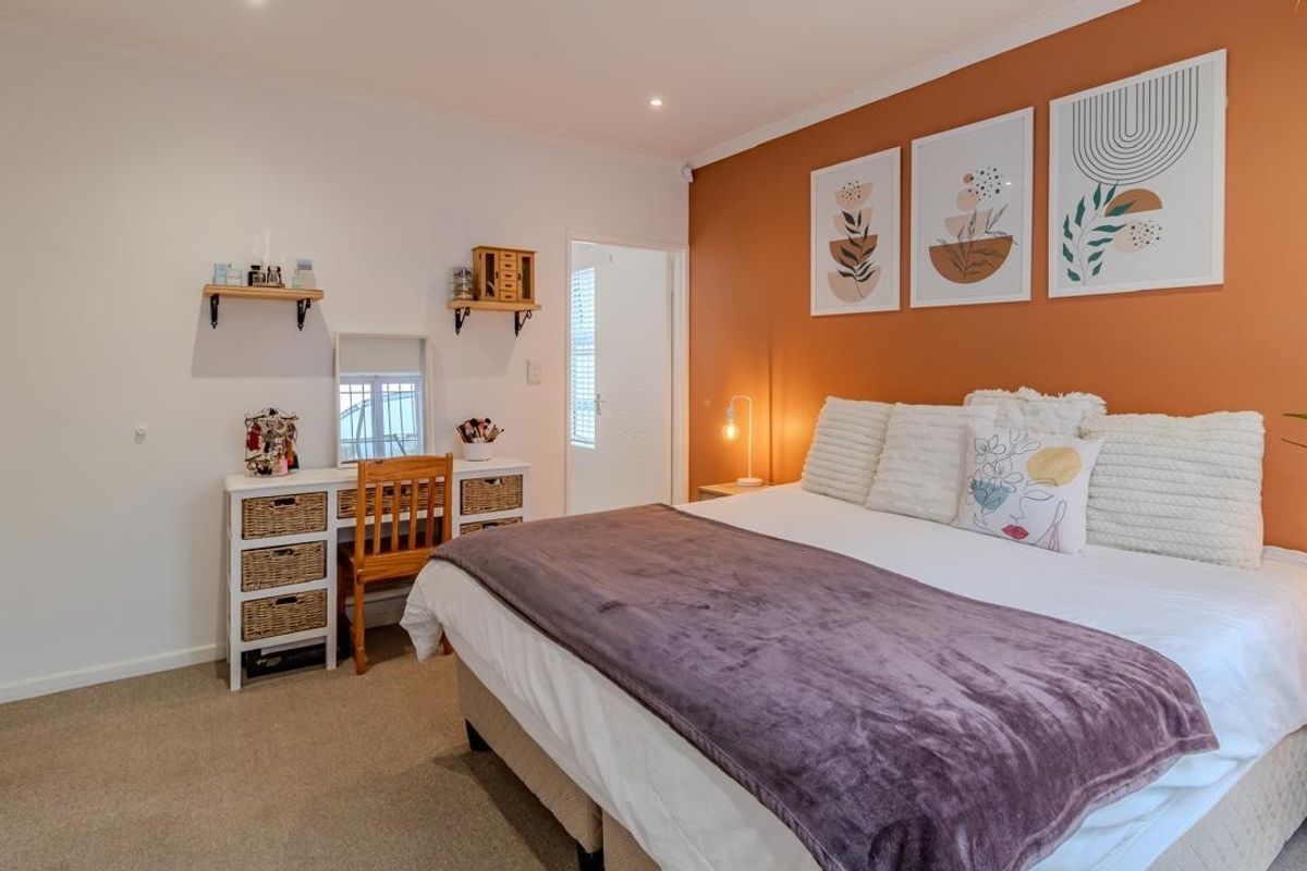 A well-maintained bedroom featuring a warm terracotta accent wall, neutral carpeting, and recessed ceiling lighting.