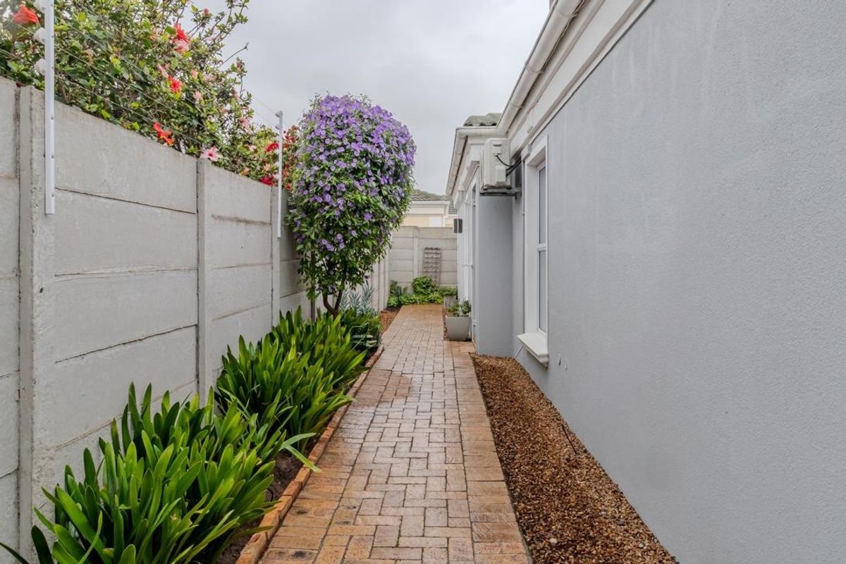 A side walkway featuring paved brick pathways, a precast concrete boundary wall, and established garden landscaping along the side of the house.