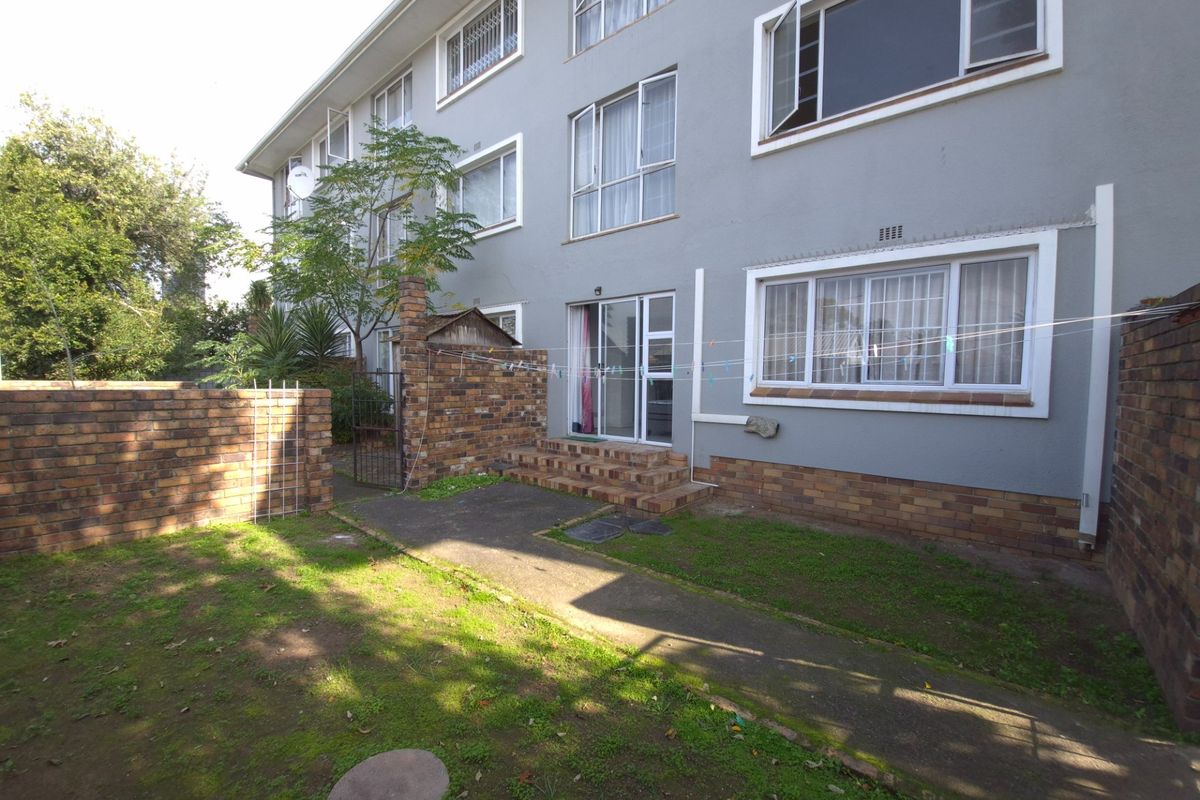 Rear view of the apartment building featuring a private garden area, brick boundary walls, and direct access via sliding glass doors.