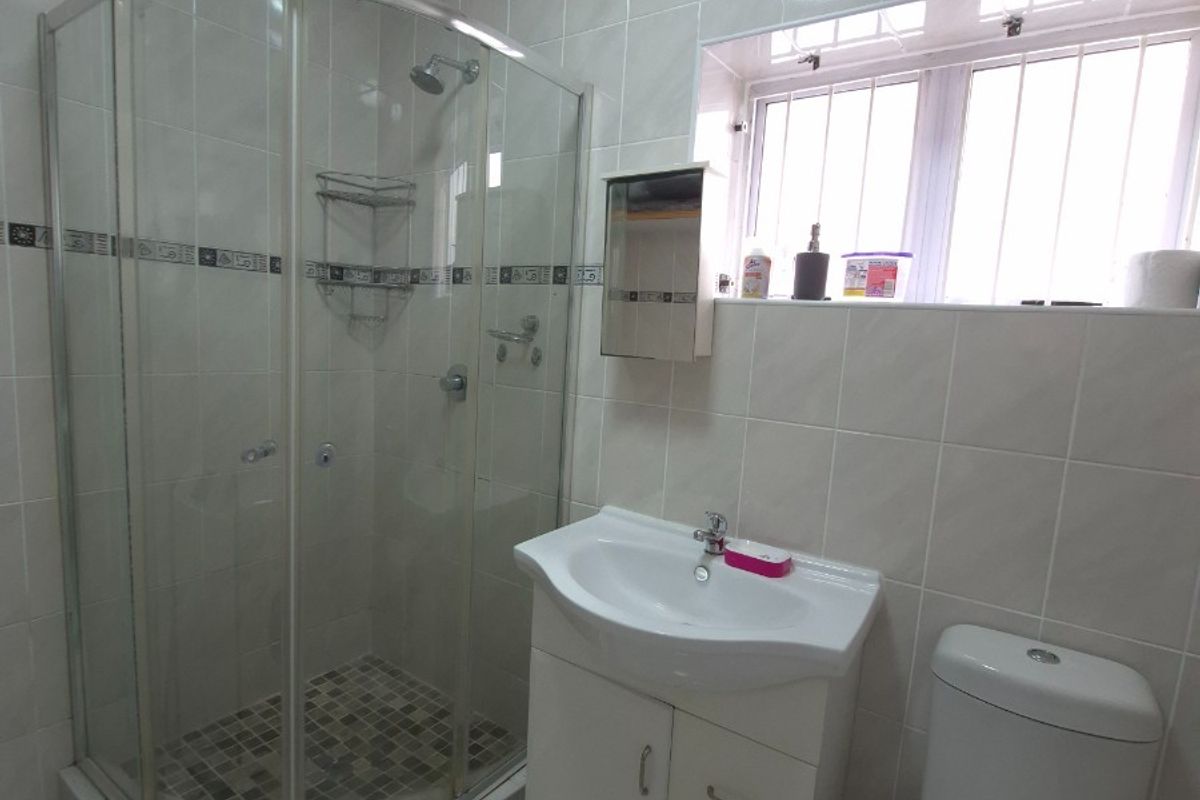 A functional bathroom featuring a corner shower enclosure, a vanity basin with storage, a toilet, and tiled walls and flooring.