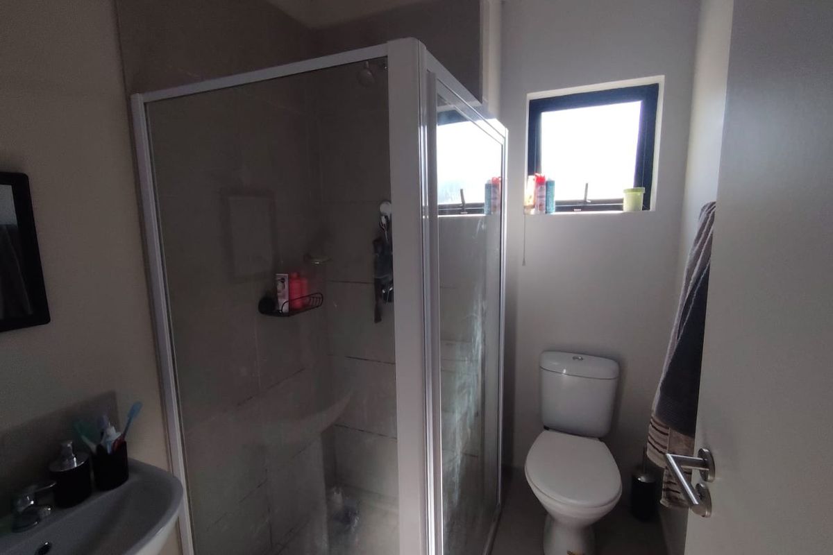 Compact bathroom featuring a corner shower enclosure, pedestal basin, and toilet with tiled flooring and natural light from a small window.