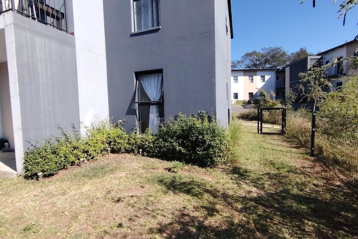 A view of the rear exterior of the apartment building, featuring a private garden area with a small lawn and perimeter fencing.