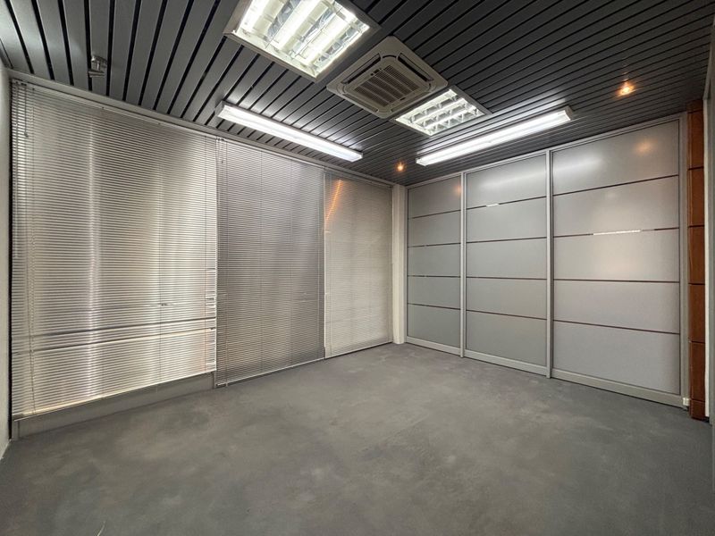 A modern, empty office space featuring a slatted metal ceiling, recessed lighting, integrated air conditioning, and sleek sliding glass partitions.