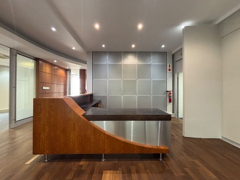 A professional office reception area featuring a modern built-in desk, wood flooring, and recessed lighting in a clean, well-maintained space.