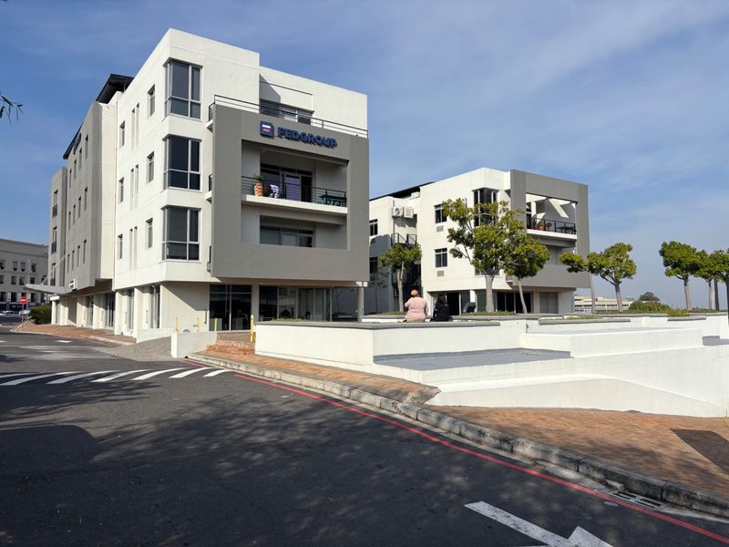 Modern multi-story office complex featuring contemporary architectural design, balconies, and paved exterior grounds with integrated retaining walls.