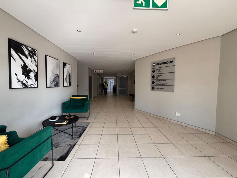 A bright and professional office building hallway featuring ceramic floor tiles, recessed lighting, and a wall-mounted directory sign for tenants.