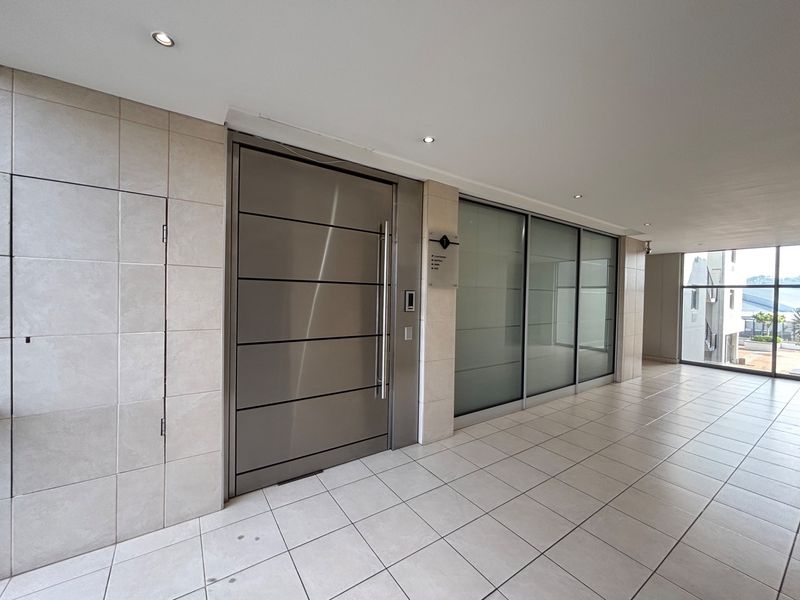 Modern office entrance featuring a sleek stainless steel pivot door, frosted glass partitioning, and clean ceramic floor tiling in a well-lit lobby area.