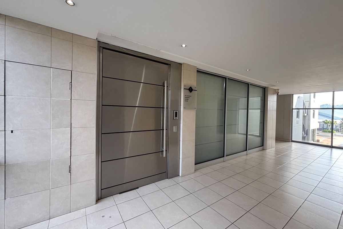 Modern office entrance featuring a sleek stainless steel pivot door, frosted glass partitioning, and clean ceramic floor tiling in a well-lit lobby area.