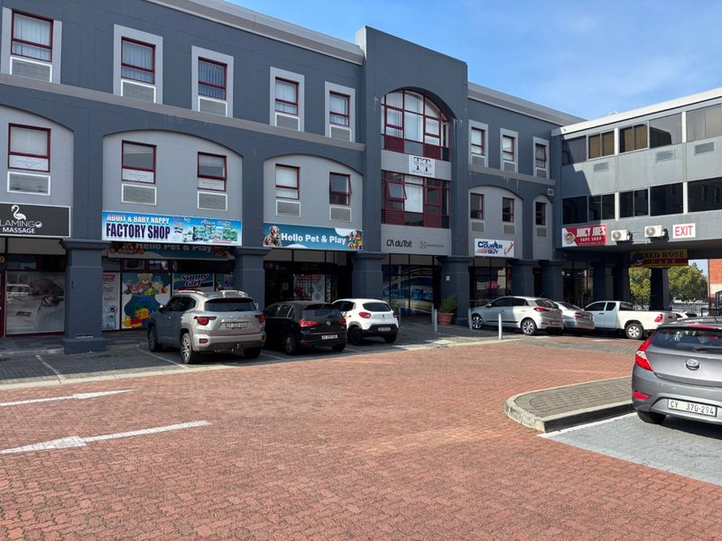 Front elevation of a multi-level commercial retail complex featuring paved parking, storefront signage, and multiple business entrances.