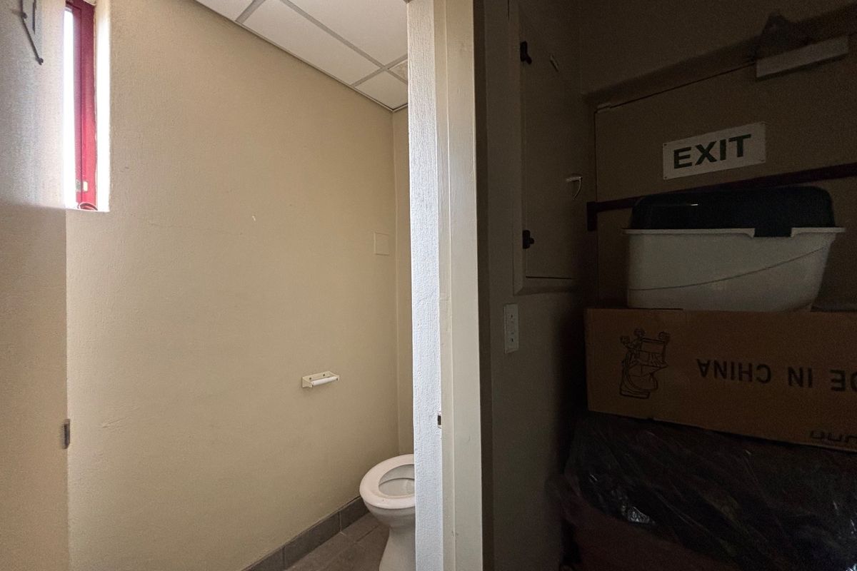 A small, functional restroom facility featuring a standard toilet and drop ceiling, currently showing signs of wear and water staining.