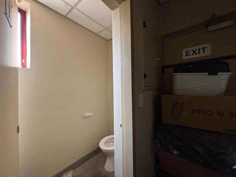A small, functional restroom facility featuring a standard toilet and drop ceiling, currently showing signs of wear and water staining.