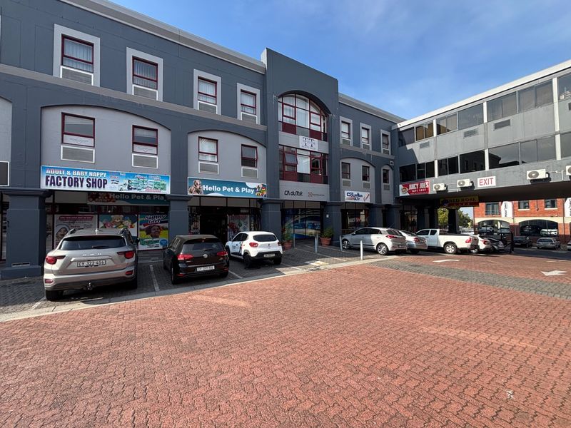 Front view of a multi-level commercial retail building featuring multiple storefronts, paved parking area, and external signage.