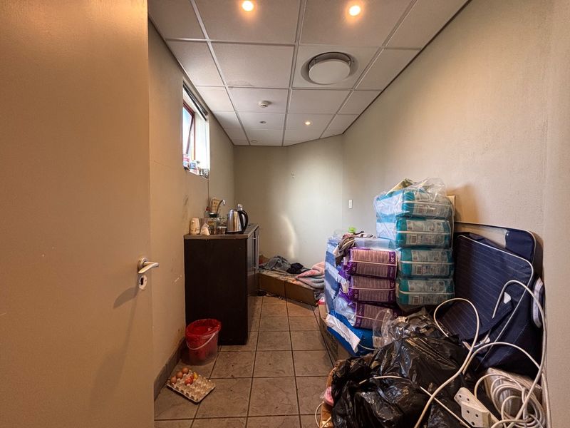 A utility space featuring tiled flooring, a drop ceiling with recessed lighting, and a small sink area with built-in cabinetry.