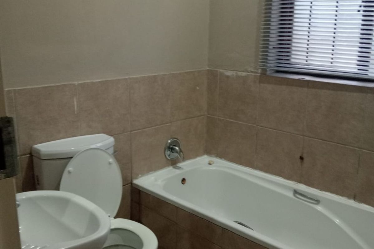 A functional bathroom featuring a pedestal basin, toilet, and bathtub with tiled finishes, requiring minor cosmetic updates to improve its overall appearance.