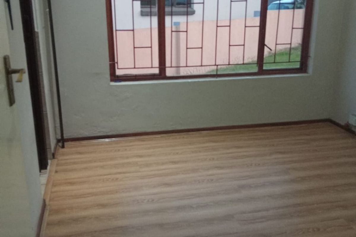 An empty bedroom featuring laminate flooring, timber-framed windows with security bars, and neutral wall finishes.