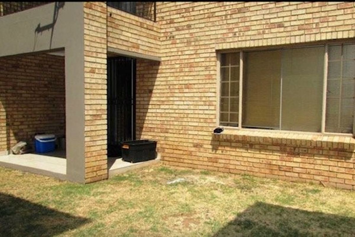 A view of the apartment's rear exterior, featuring a covered patio area, brick facade, and a small private garden space.