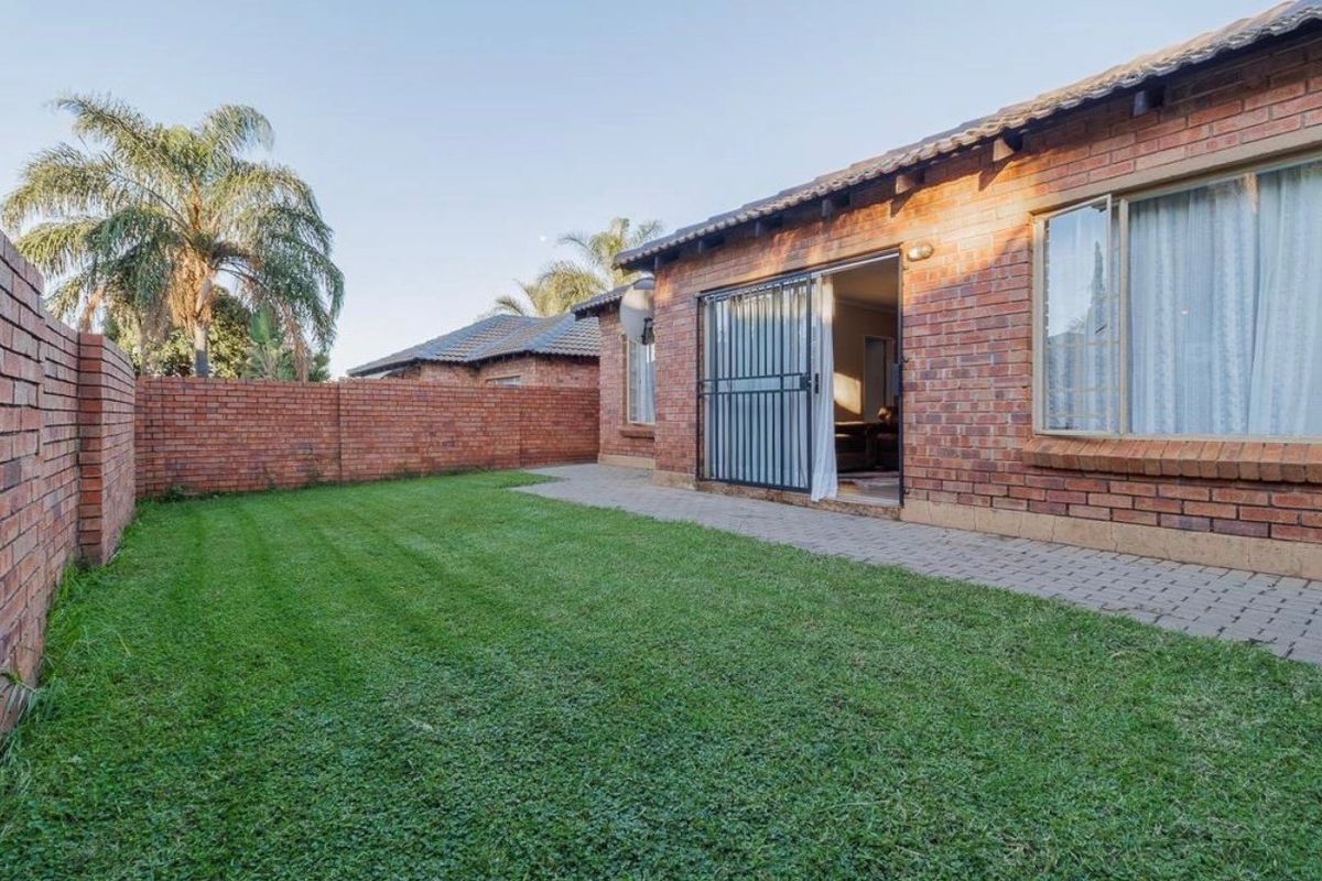 A private rear garden featuring a well-maintained lawn, paved patio area, and face-brick exterior walls with secure sliding door access.