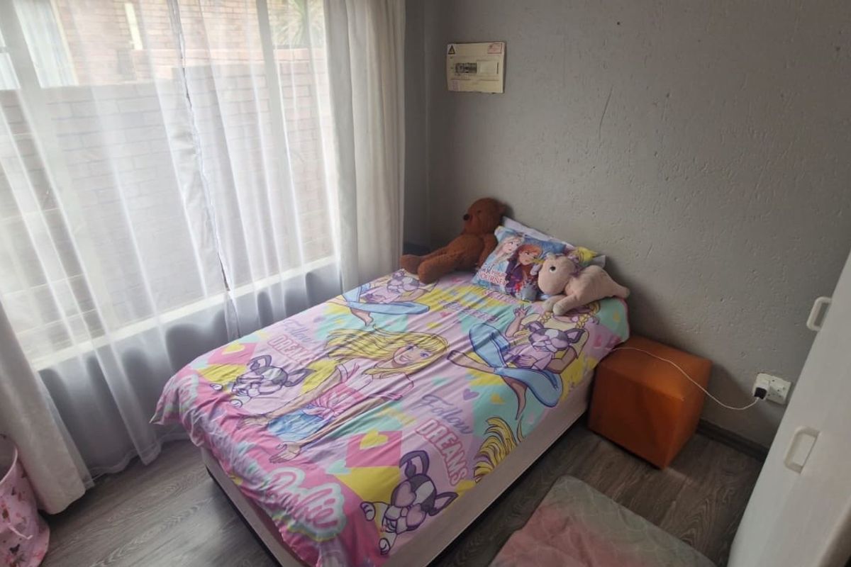 A compact bedroom featuring laminate flooring, a large window with sheer curtains, and a built-in cupboard.