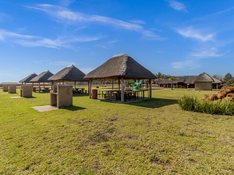 Spacious outdoor entertainment area featuring multiple thatched gazebos, built-in braai stands, and expansive lawn space, ideal for gatherings on this farm property.
