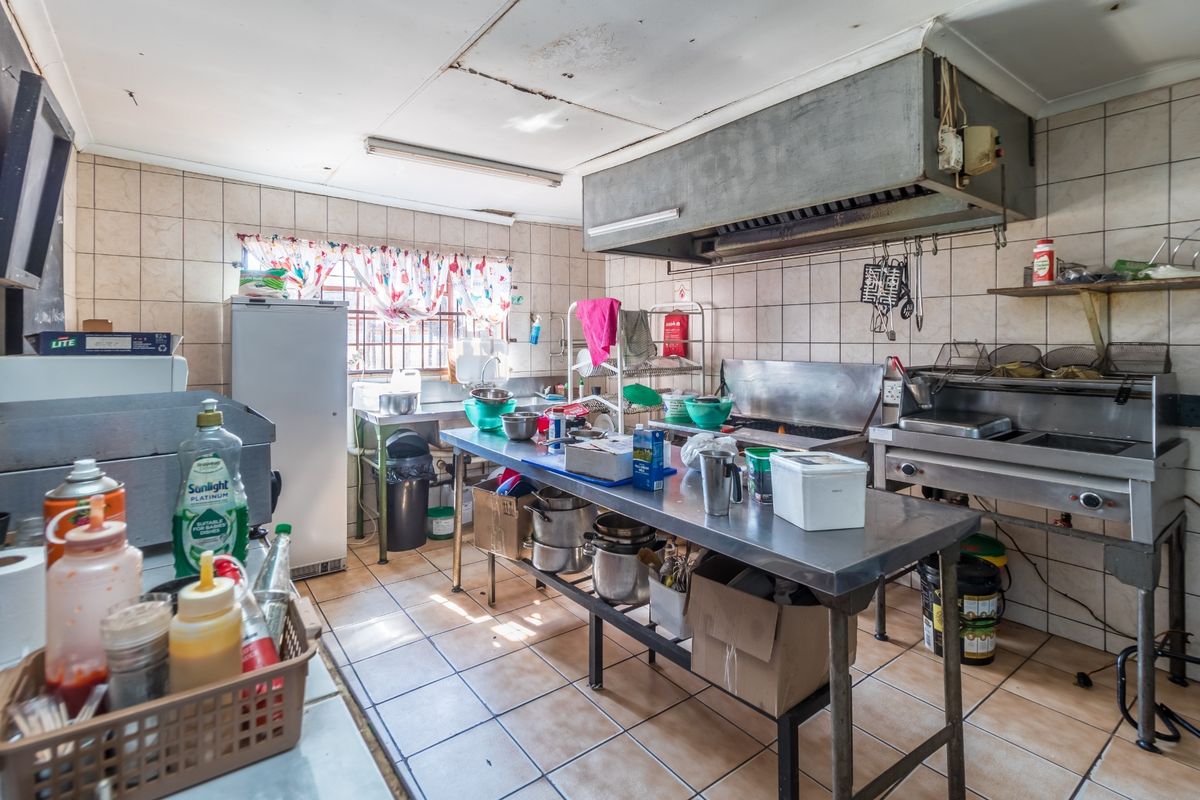 Commercial-style kitchen area featuring stainless steel work surfaces, a large industrial extractor hood, and tiled wall finishes.