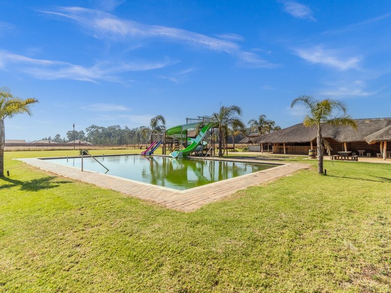 Outdoor pool area featuring a built-in swimming pool with water slides, adjacent to a large thatched-roof entertainment structure on a spacious farm property.