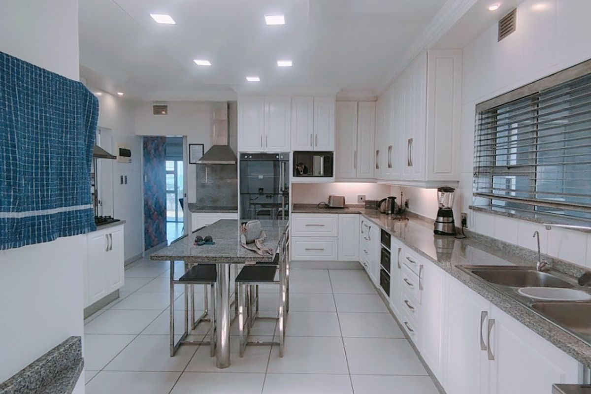 Modern kitchen featuring white cabinetry, granite countertops, a central island, built-in appliances, and bright recessed lighting with tiled flooring throughout.