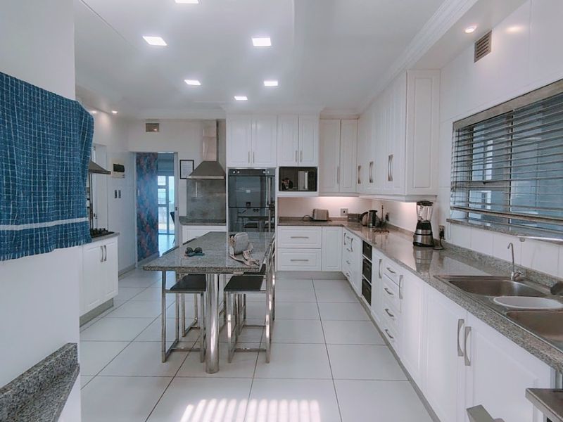 Modern kitchen featuring white cabinetry, granite countertops, a central island, built-in appliances, and bright recessed lighting with tiled flooring throughout.