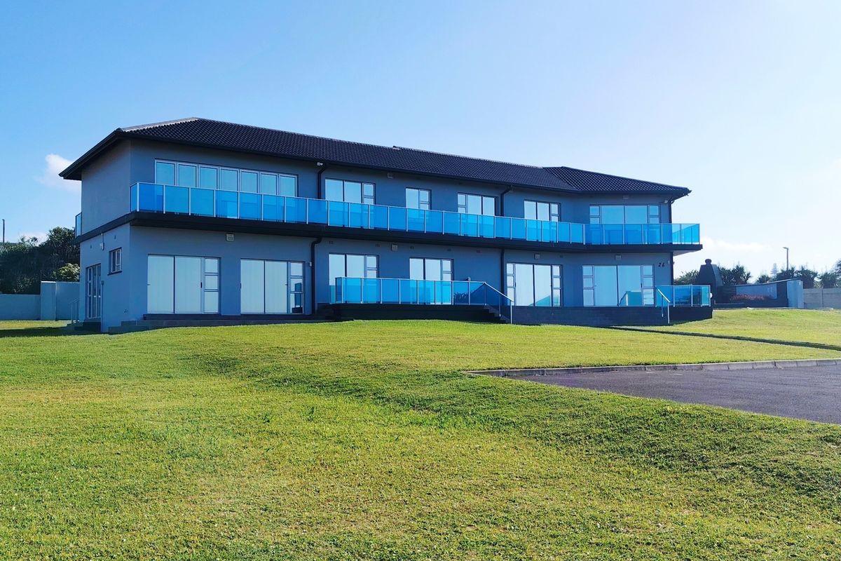 A modern two-story residential building featuring extensive glass balustrades, large sliding doors, and a well-maintained lawn area.
