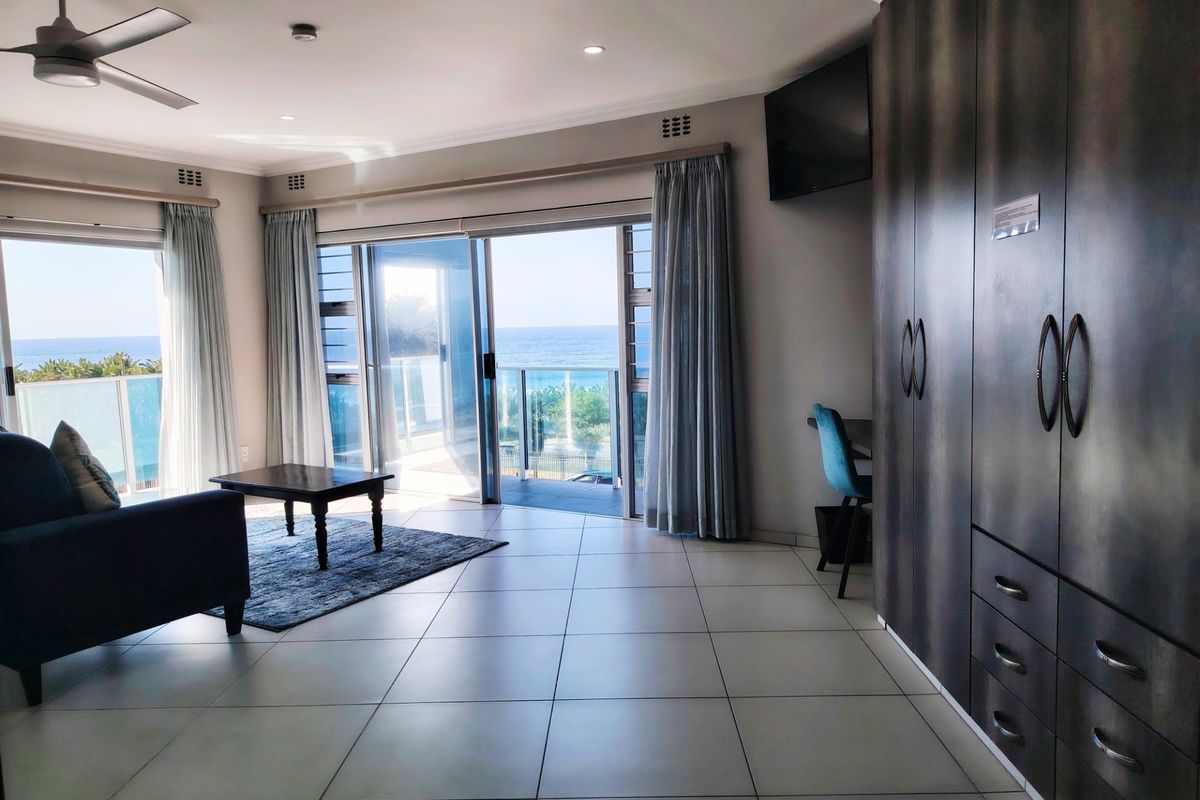 Spacious living area featuring large sliding glass doors with ocean views, tiled flooring, built-in cabinetry, and a ceiling fan.