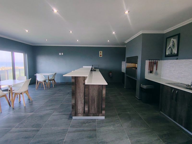 Spacious open-plan entertainment area featuring a built-in braai, modern kitchen island with stone countertops, and large sliding doors leading to an outdoor view.